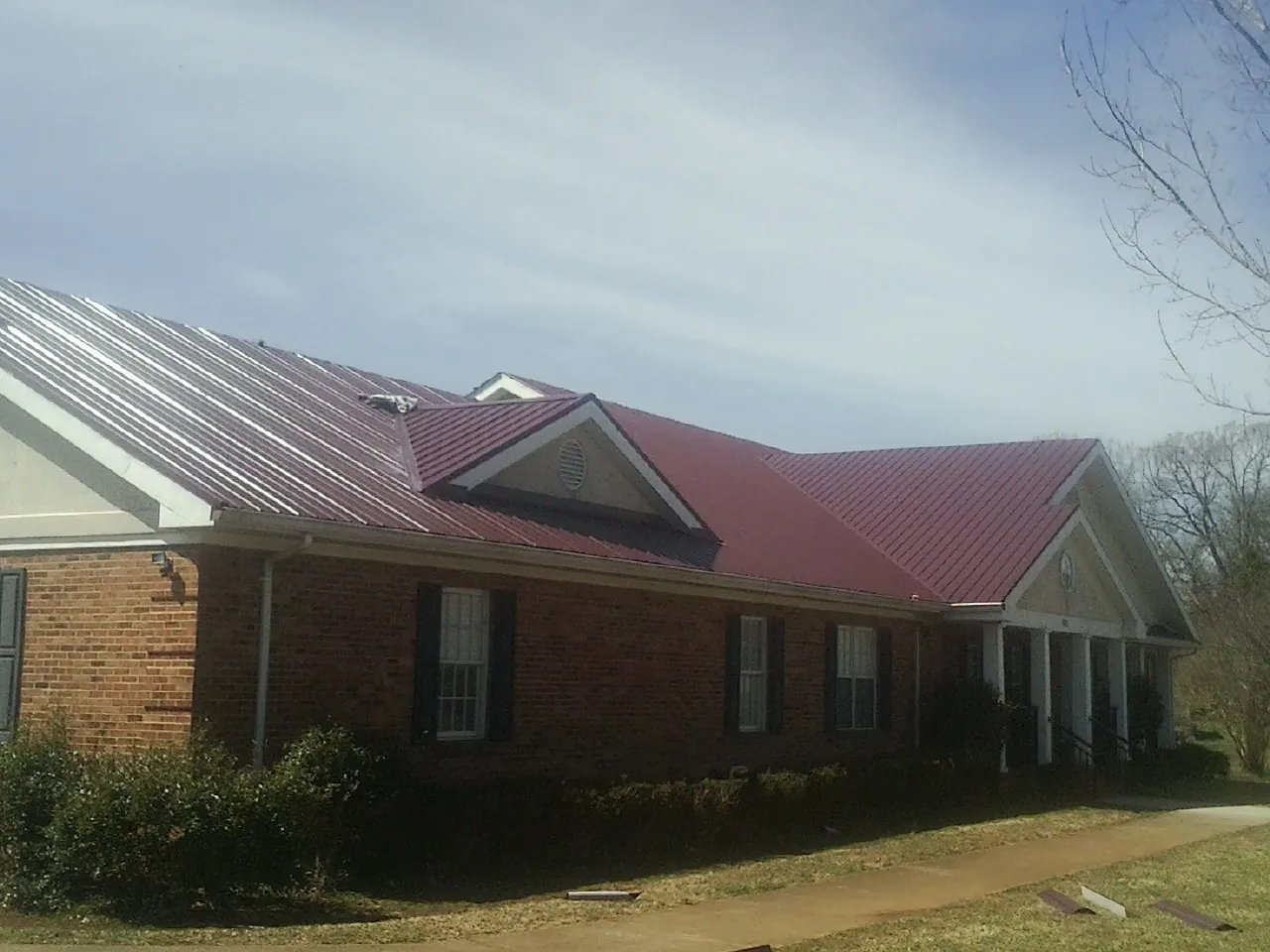 Red metal roof with gabled entries on a long brick building, from a Hail Damage Roof Repair job in Nottingham